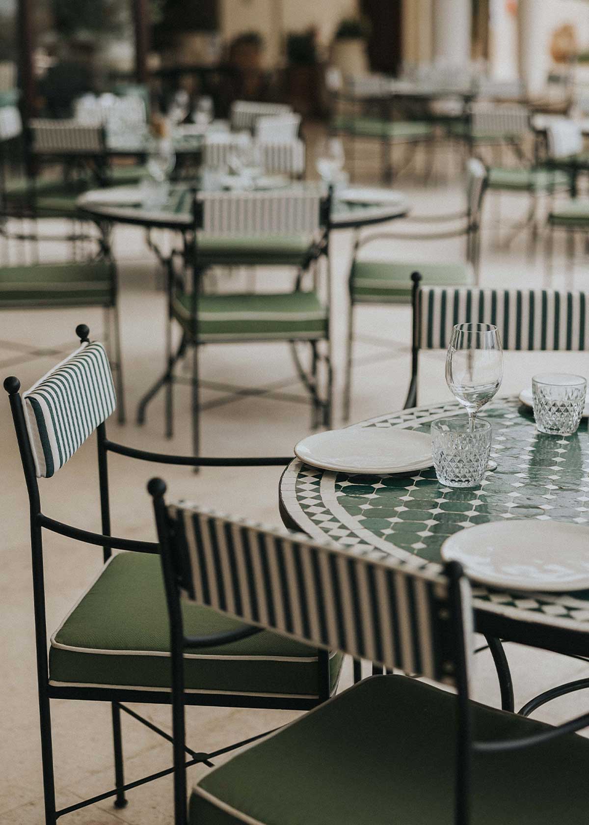 Mesa de exterior circular con estructura de hierro forjado acabado en negro y sobre en mosaico de azulejos.