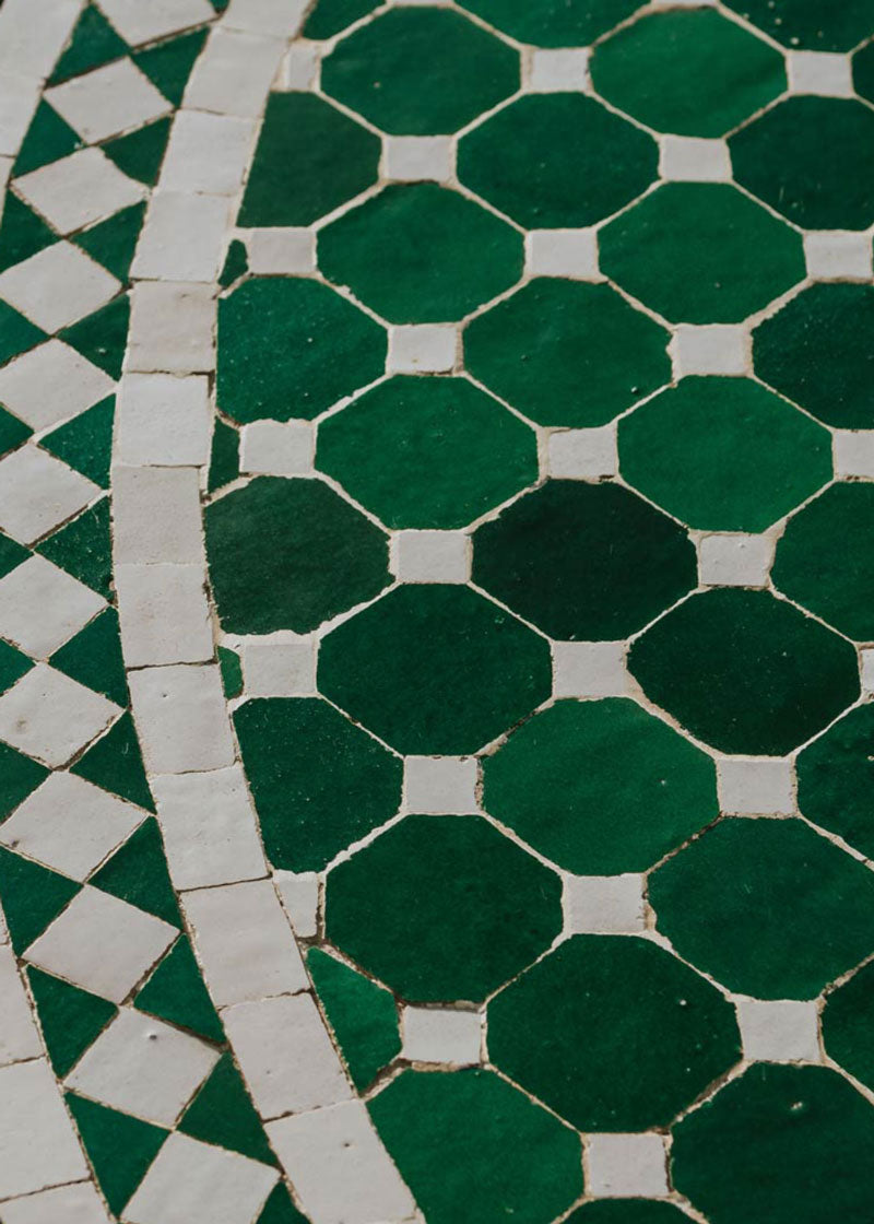 Mesa de exterior circular con estructura de hierro forjado acabado en negro y sobre en mosaico de azulejos.