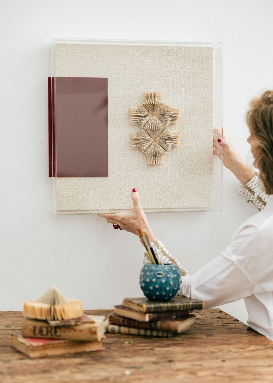 Escultura de pared forrada en lino rústico con caja de metacrilato transparente. Está formada por una serie de libros plegados y formas geométricas en metacrilato