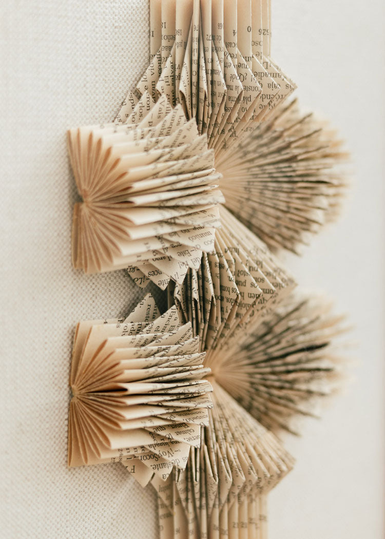 Escultura de pared forrada en lino rústico con caja de metacrilato transparente. Está formada por una serie de libros plegados y formas geométricas en metacrilato