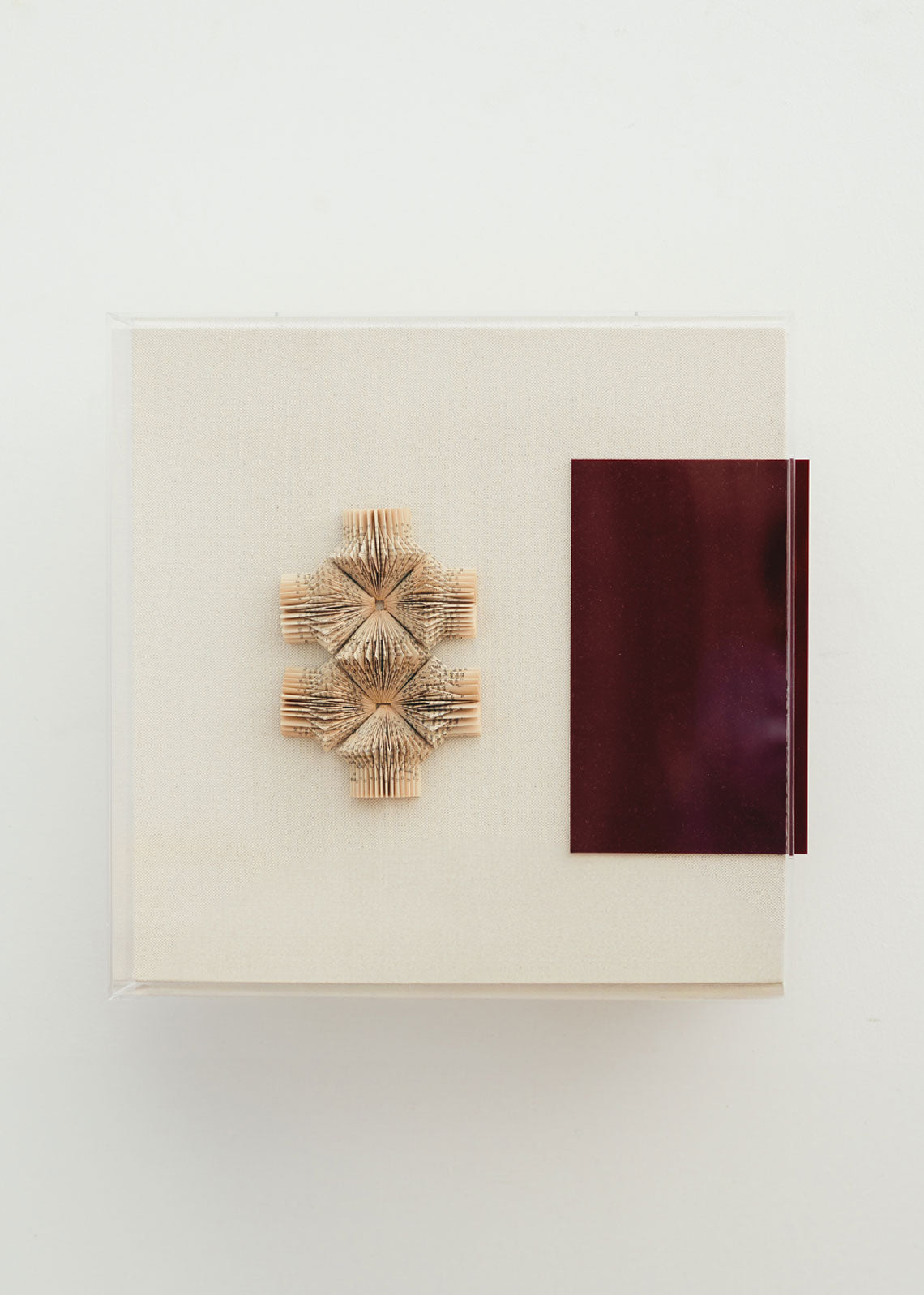 Escultura de pared forrada en lino rústico con caja de metacrilato transparente. Está formada por una serie de libros plegados y formas geométricas en metacrilato