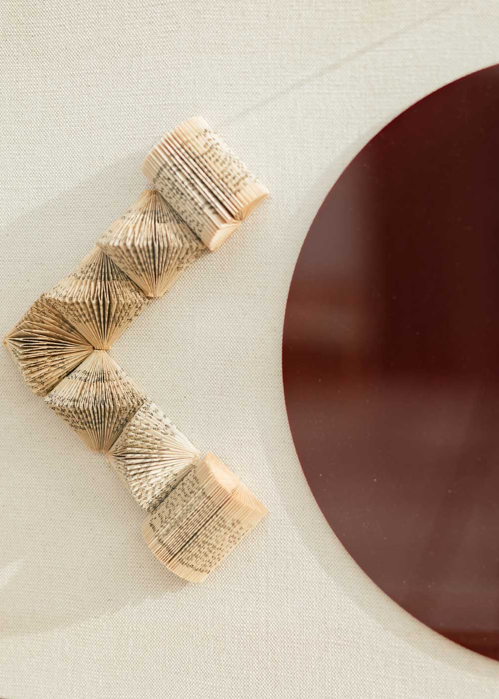 Escultura de pared forrada en lino rústico con caja de metacrilato transparente. Está formada por una serie de libros plegados y formas geométricas en metacrilato.