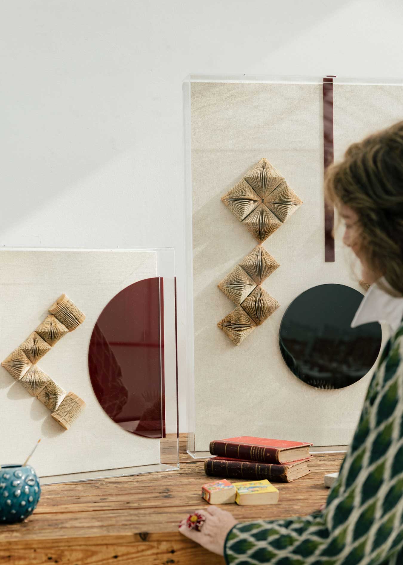 Escultura de pared forrada en lino rústico con caja de metacrilato transparente. Está formada por una serie de libros plegados y formas geométricas en metacrilato.