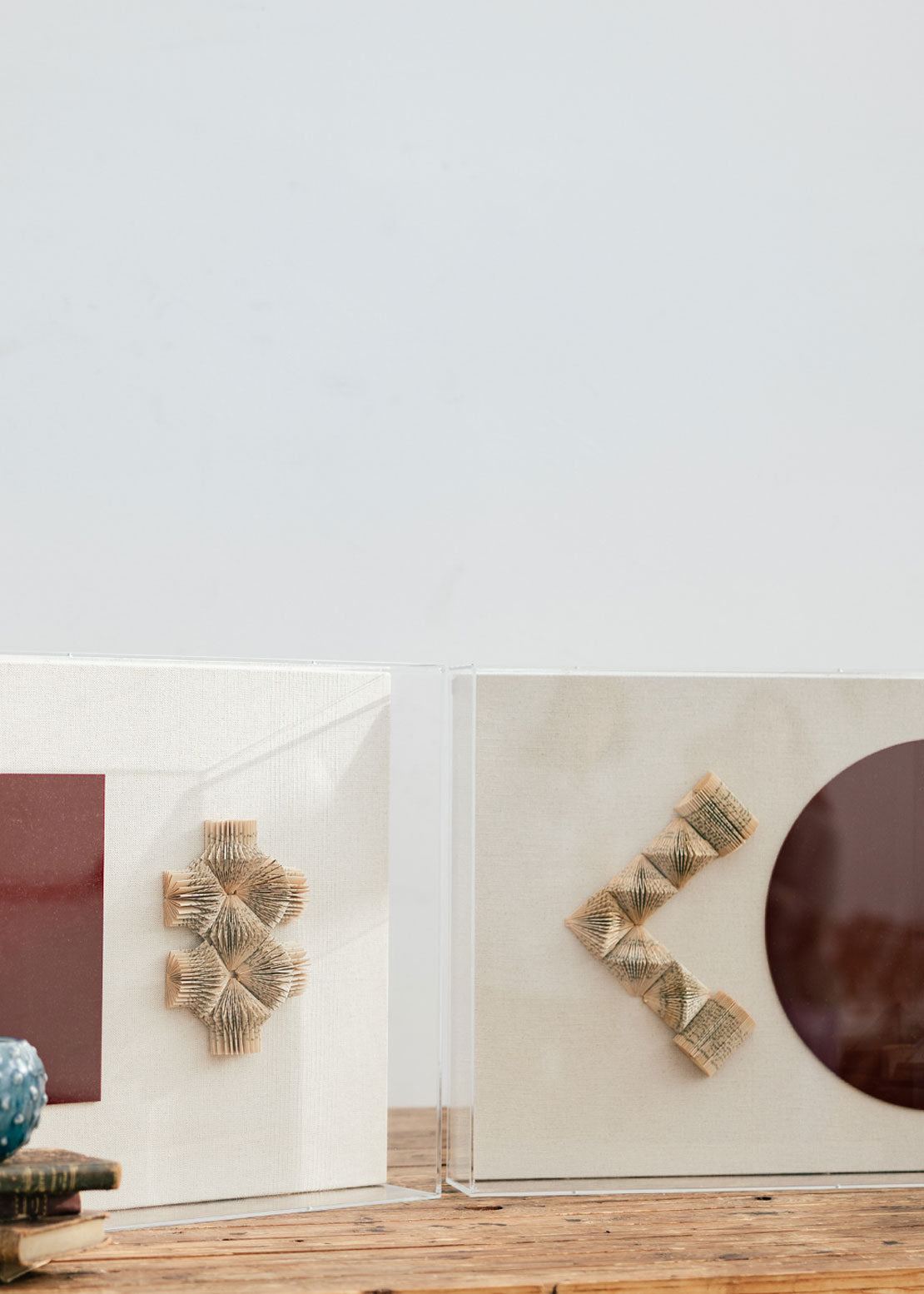 Escultura de pared forrada en lino rústico con caja de metacrilato transparente. Está formada por una serie de libros plegados y formas geométricas en metacrilato.