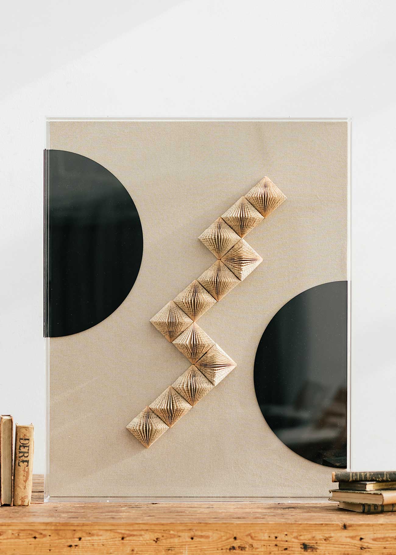 Escultura de pared forrada en lino rústico con caja de metacrilato transparente. Está formada por una serie de libros plegados y formas geométricas en metacrilato.