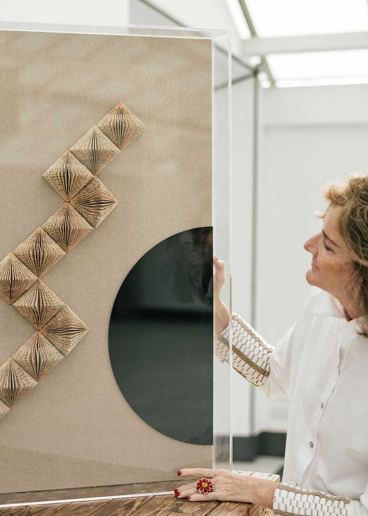 Escultura de pared forrada en lino rústico con caja de metacrilato transparente. Está formada por una serie de libros plegados y formas geométricas en metacrilato.