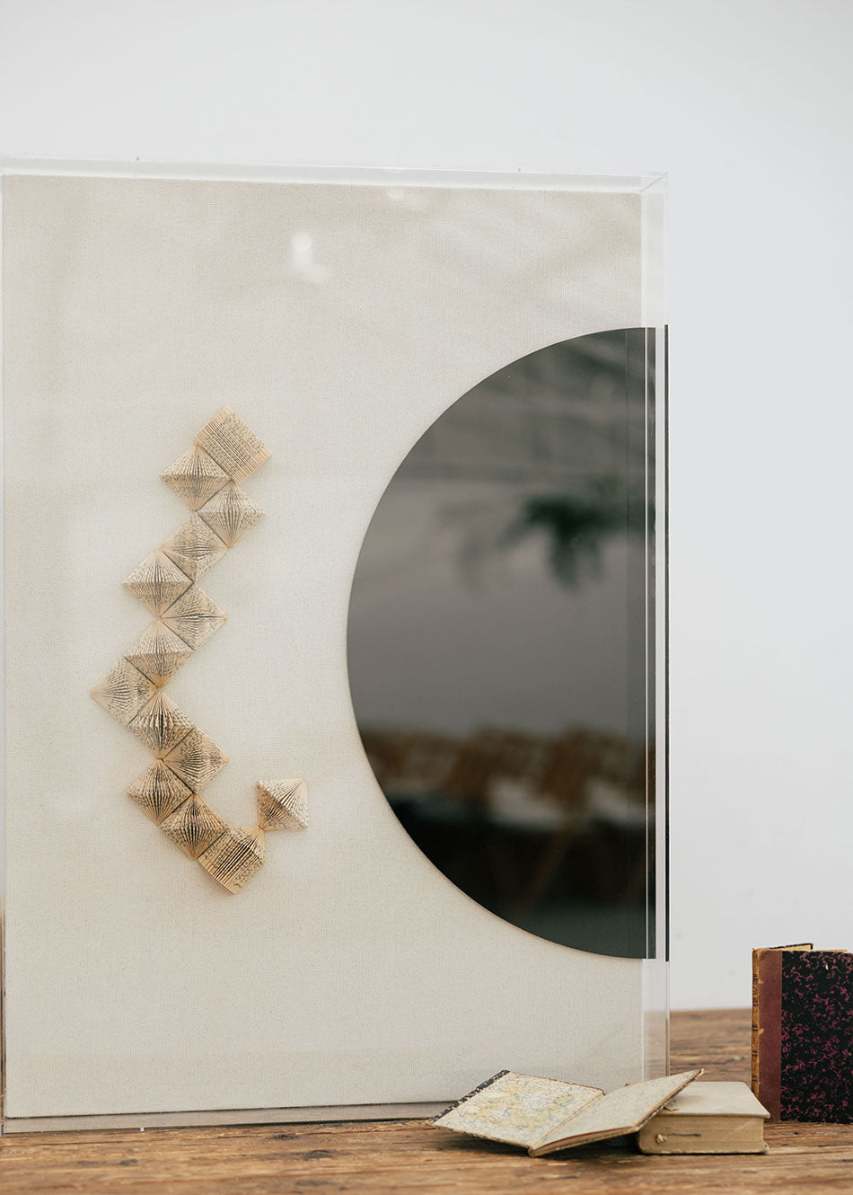 Escultura de pared en dos piezas forradas en lino rústico con cajas de metacrilato transparente. Está formada por una serie de libros plegados y formas geométricas en metacrilato.