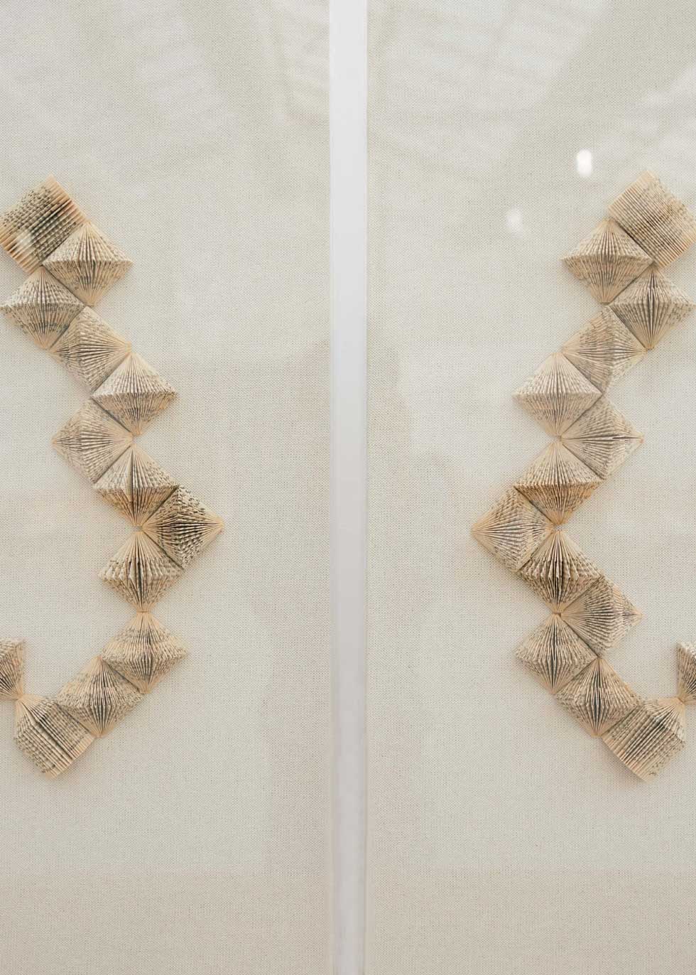Escultura de pared en dos piezas forradas en lino rústico con cajas de metacrilato transparente. Está formada por una serie de libros plegados y formas geométricas en metacrilato.