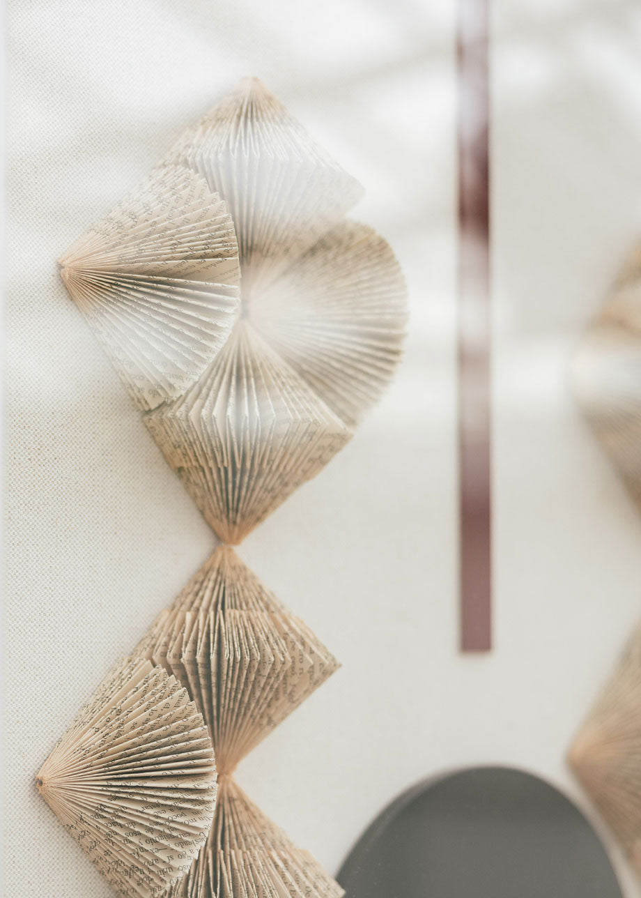 Escultura de pared forrada en lino rústico con caja de metacrilato transparente. Está formada por una serie de libros plegados y formas geométricas en metacrilato
