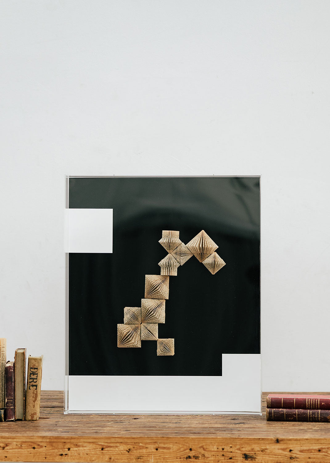 Escultura de pared forrada en metacrilato negro y blanco con caja de metacrilato transparente y serie de libros plegados.