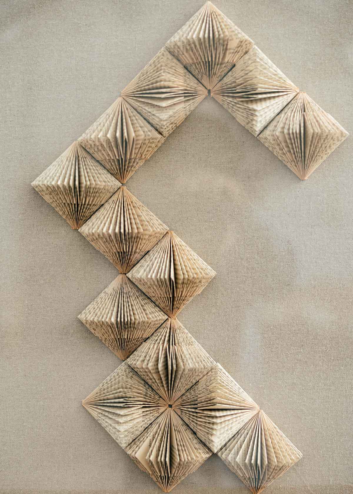 Escultura de pared forrada en lino rústico con caja de metacrilato transparente y serie de libros plegados.