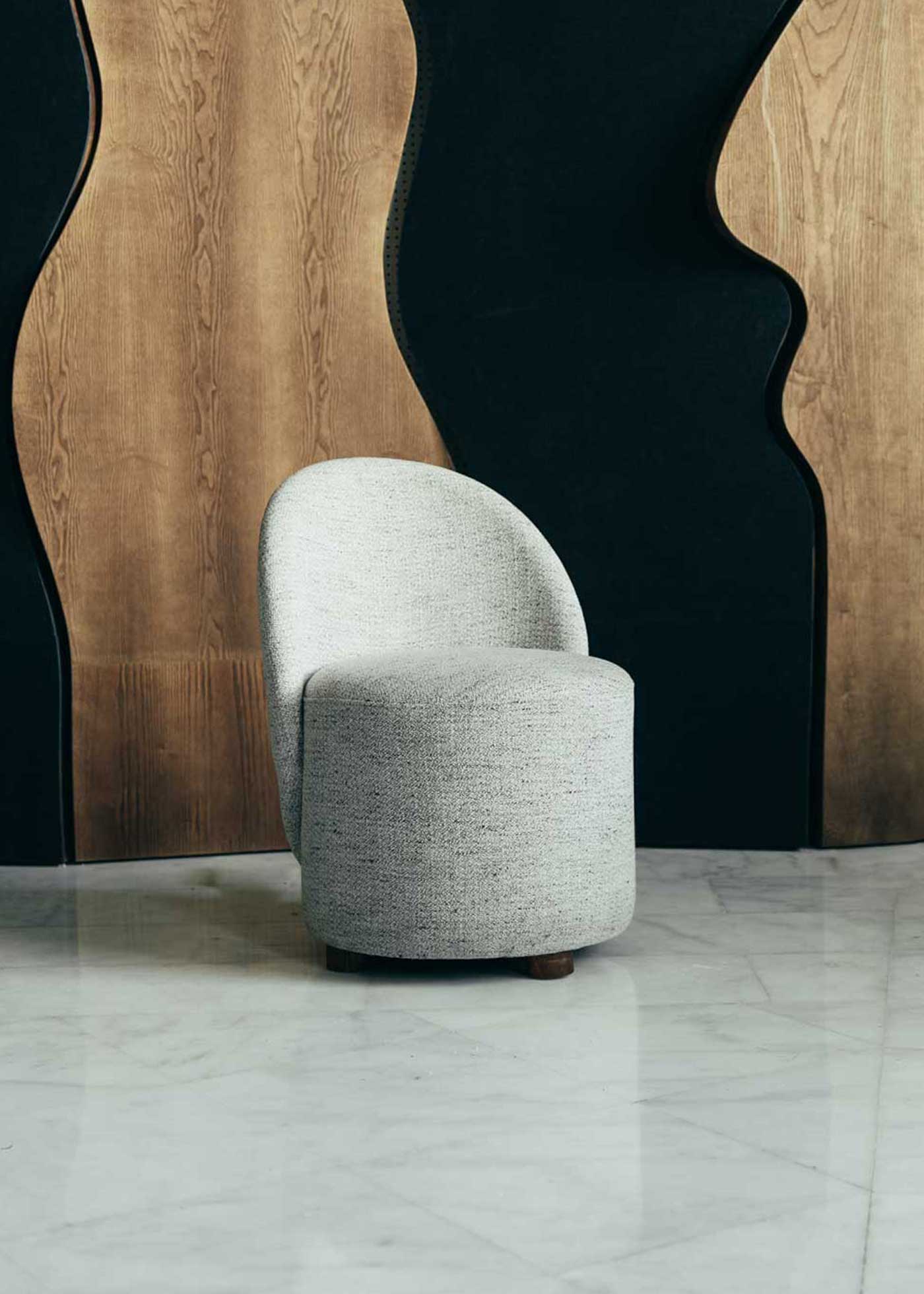Butaca con estructura de madera tapizada con tela jaspeada en tonos crudos y patas de madera.