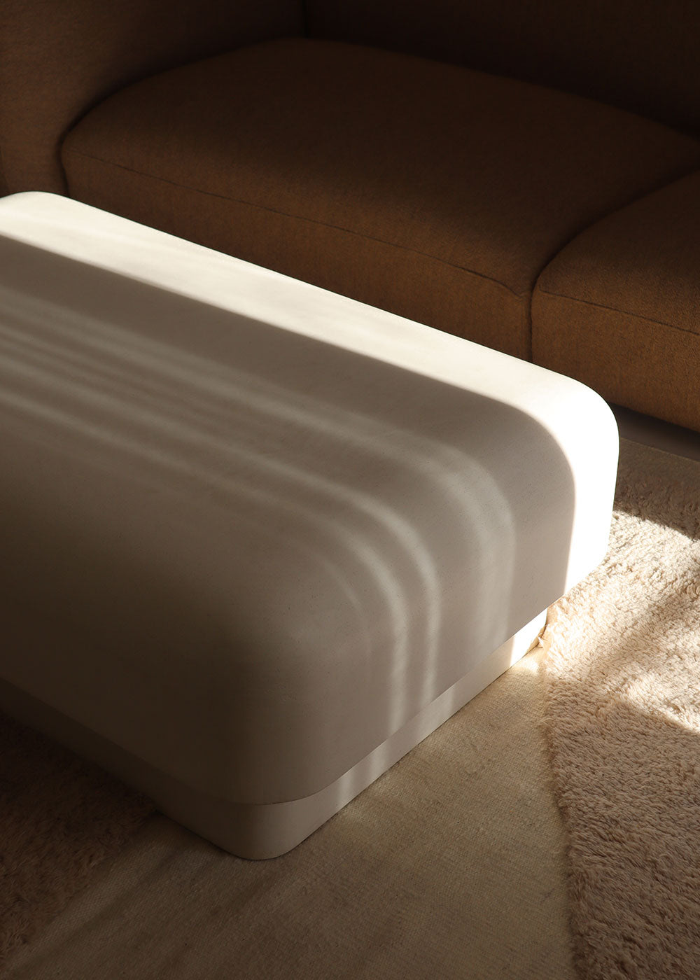 Mesa baja de centro con estructura de madera revestida de estuco en color crudo.