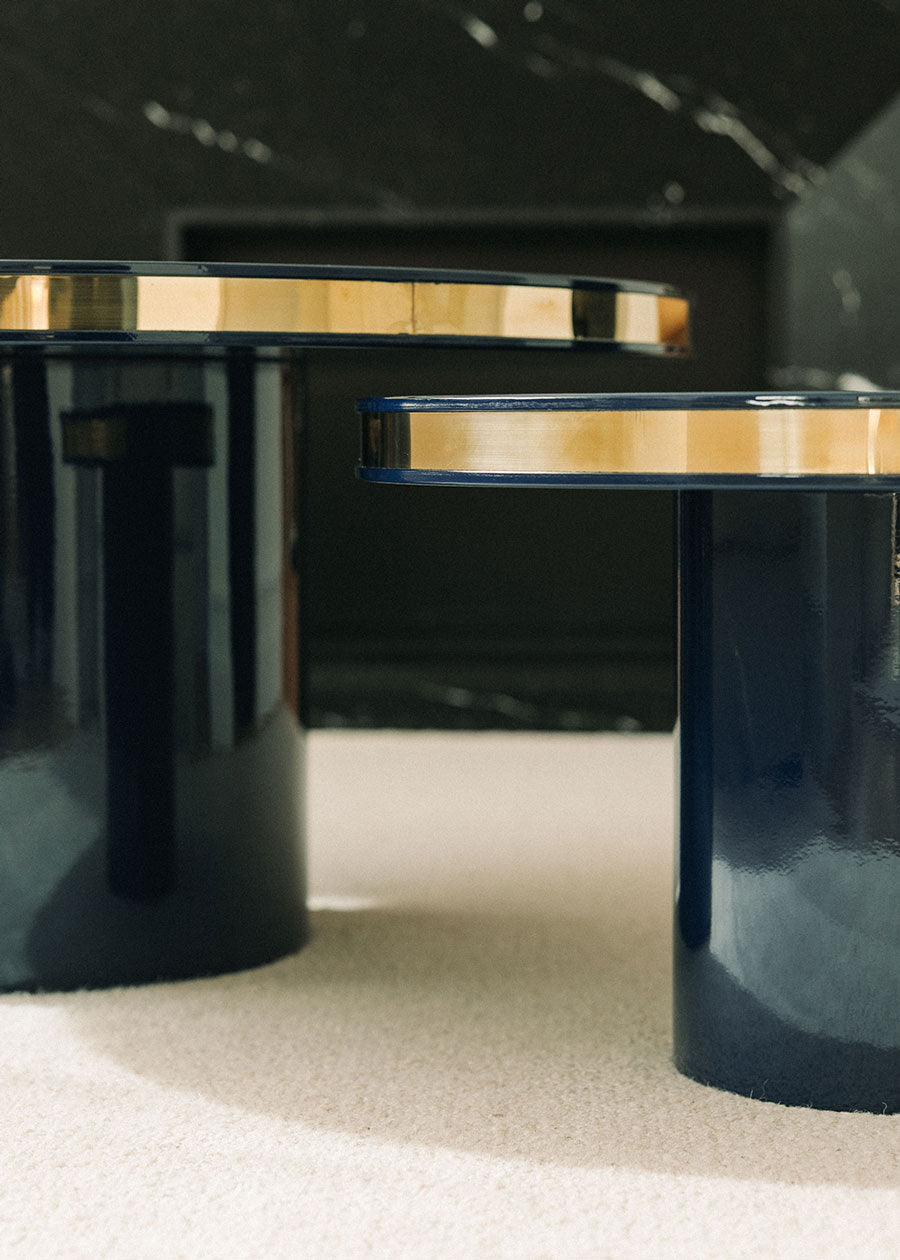 Conjunto de dos mesas circulares realizadas en madera lacadas en color negro con acabado brillo y detalle de latón.