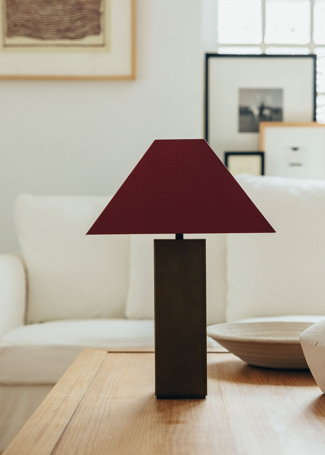 Lámpara de mesa escultórica con base y pantalla metálicas. Base en latón envejecido y pantalla lacada en dos tonos: rojo Burdeos en la cara exterior y color maquillaje en la interior.