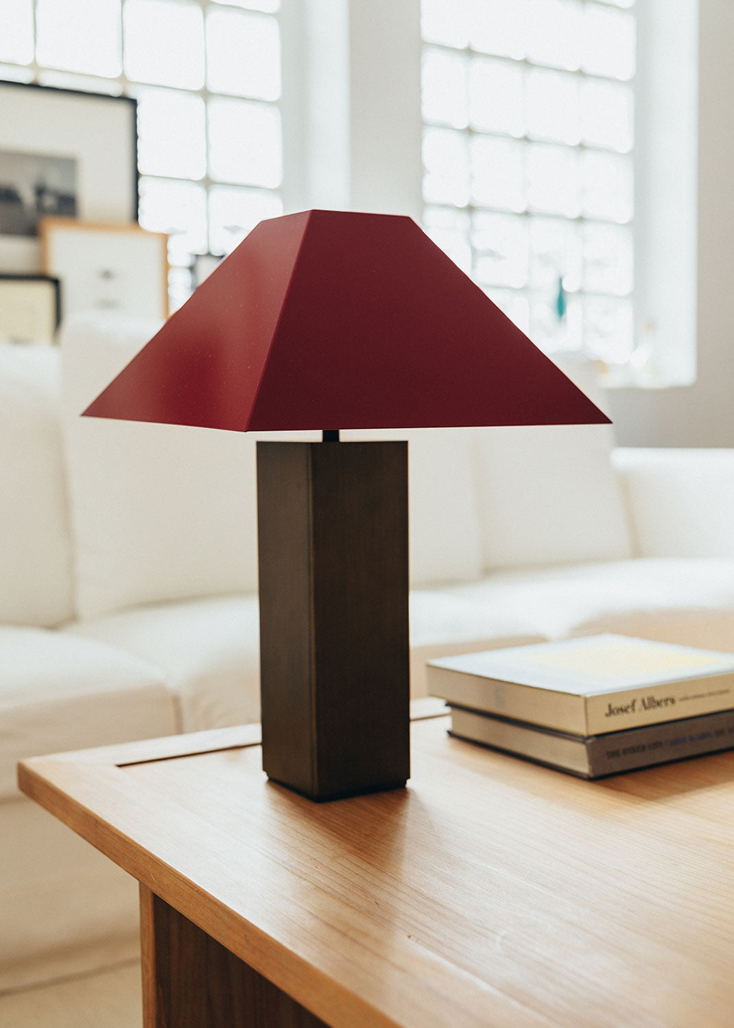 Lámpara de mesa escultórica con base y pantalla metálicas. Base en latón envejecido y pantalla lacada en dos tonos: rojo Burdeos en la cara exterior y color maquillaje en la interior.
