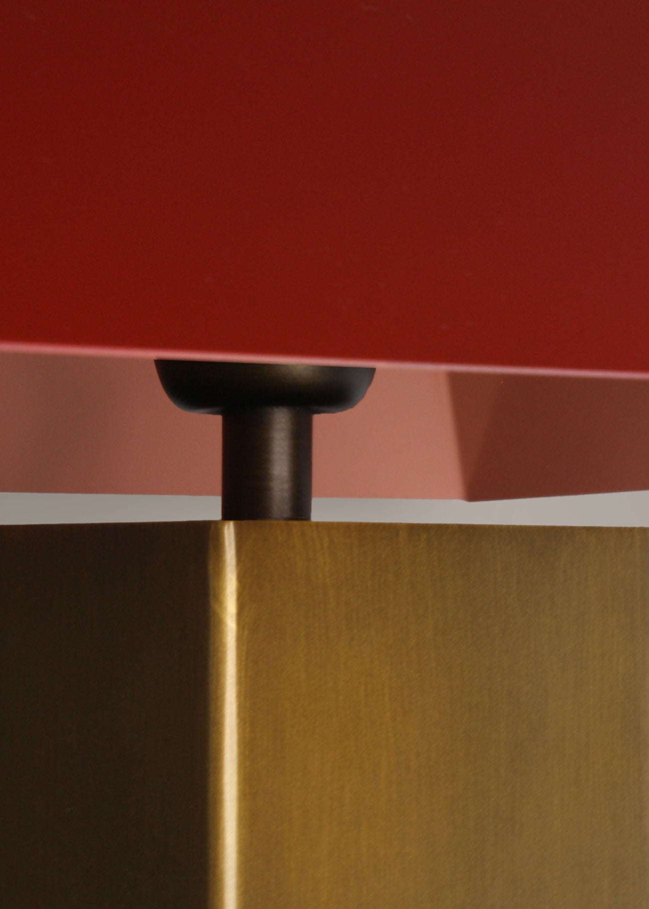 Lámpara de mesa escultórica con base y pantalla metálicas. Base en latón envejecido y pantalla lacada en dos tonos: rojo Burdeos en la cara exterior y color maquillaje en la interior.