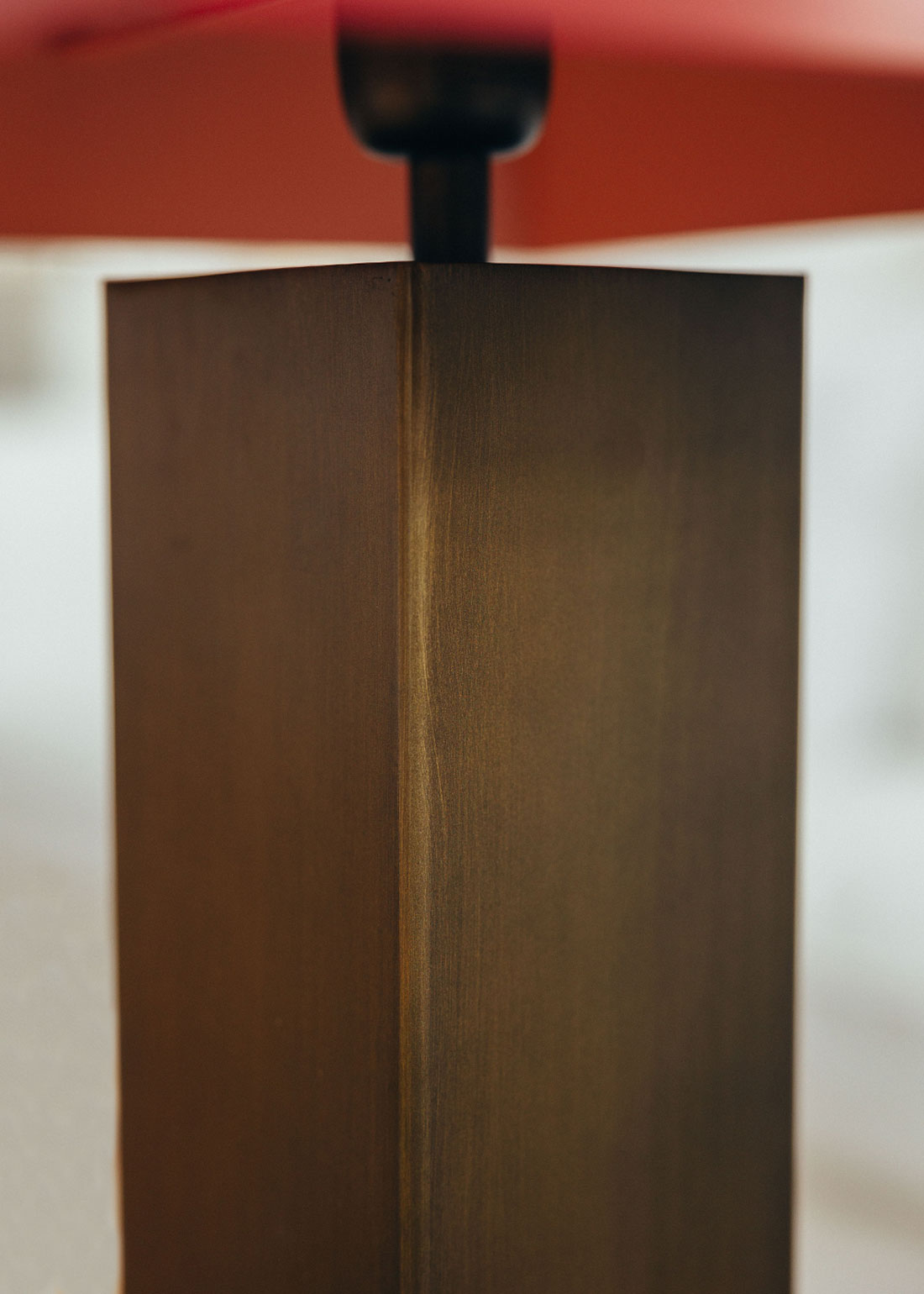 Lámpara de mesa escultórica con base y pantalla metálicas. Base en latón envejecido y pantalla lacada en dos tonos: rojo Burdeos en la cara exterior y color maquillaje en la interior.