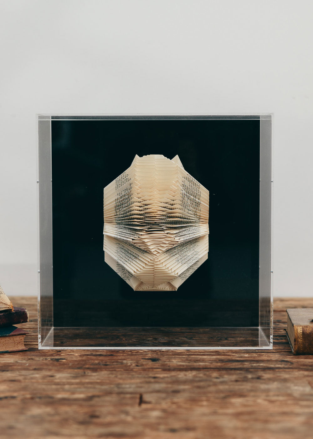 Escultura de pared forrada en metacrilato negro con caja de metacrilato transparente y libro plegado.