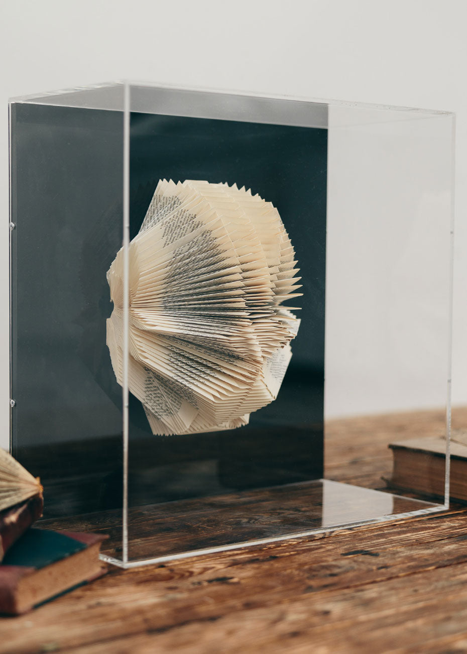 Escultura de pared forrada en metacrilato negro con caja de metacrilato transparente y libro plegado.