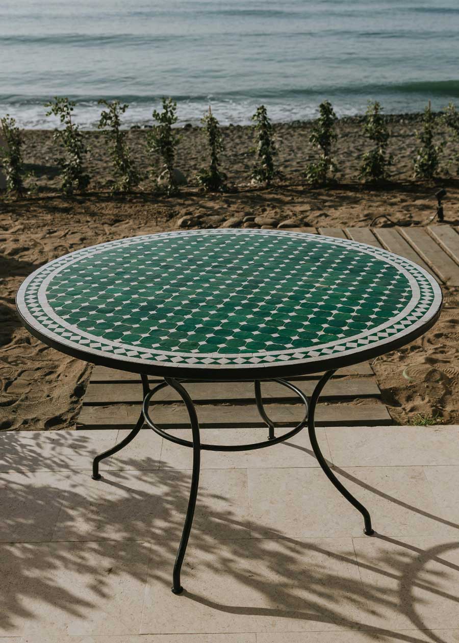 Mesa de exterior circular con estructura de hierro forjado acabado en negro y sobre en mosaico de azulejos.