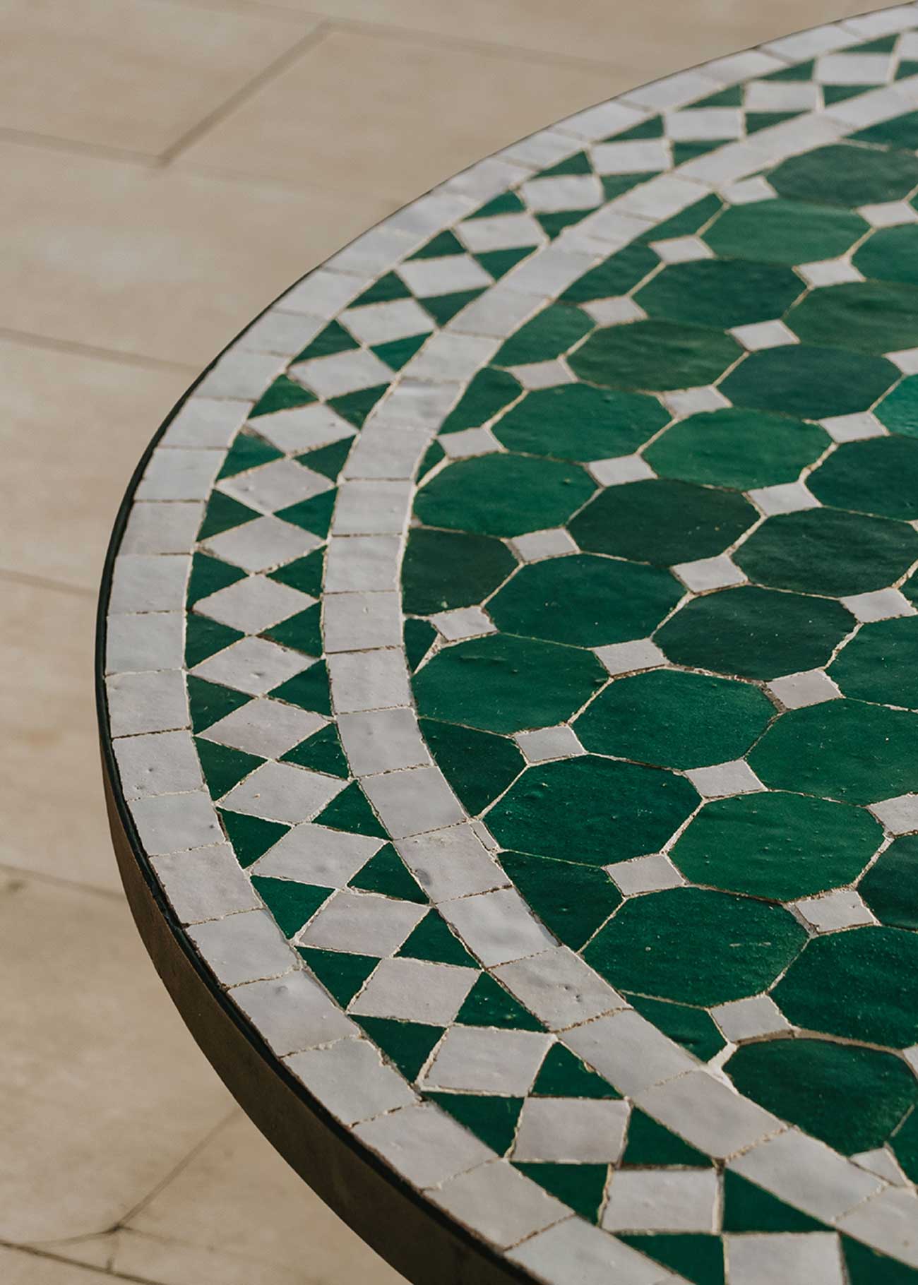 Mesa de exterior circular con estructura de hierro forjado acabado en negro y sobre en mosaico de azulejos.