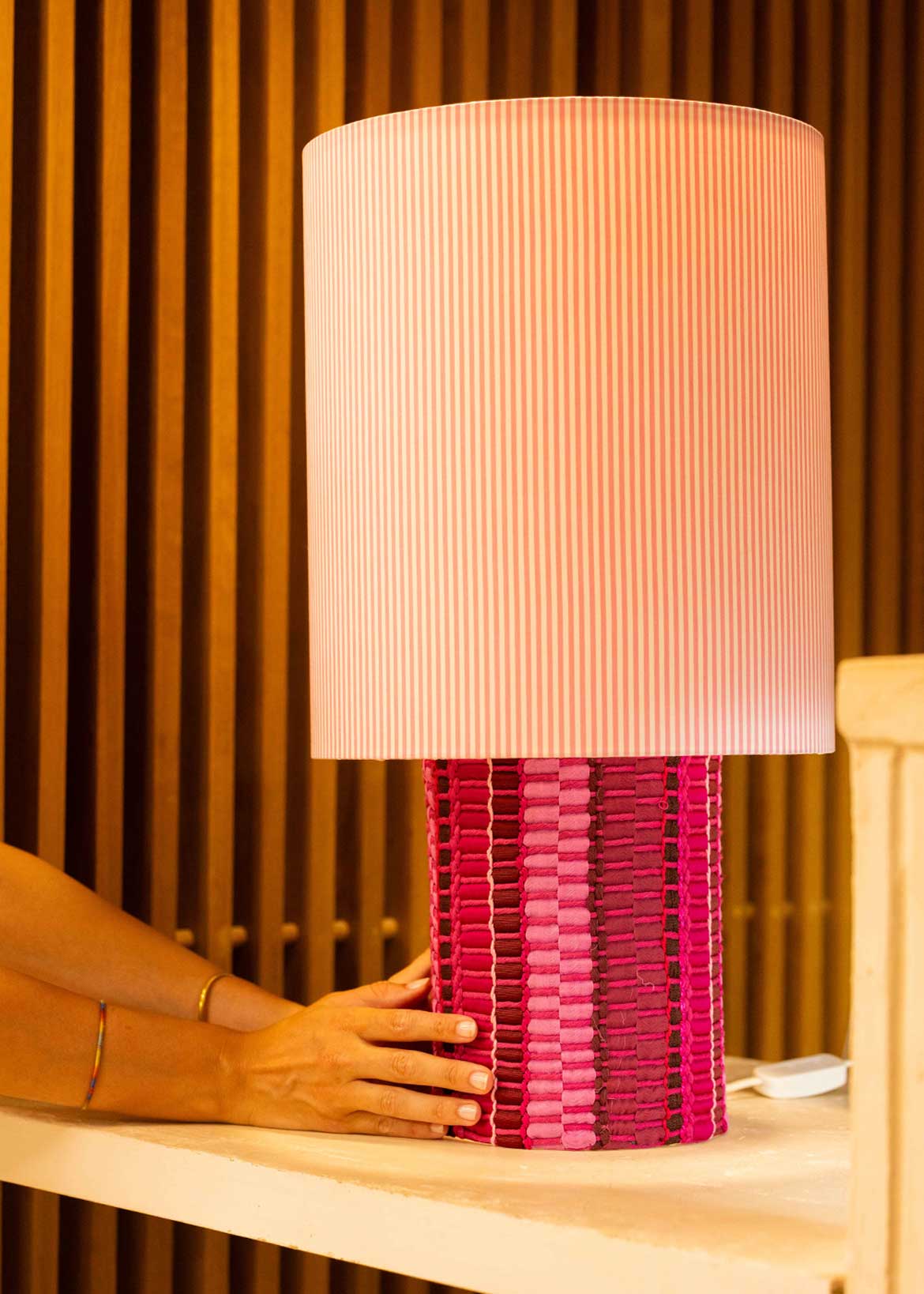 La lámpara N05 es una explosión de color. Perfecta para dar un toque de diversión y diseño a cualquier espacio. Con una base cubierta de tejido hecho en telar, combinando sedas, linos y diferentes texturas y una maxi pantalla de tejido de oxford de rayas rosas.