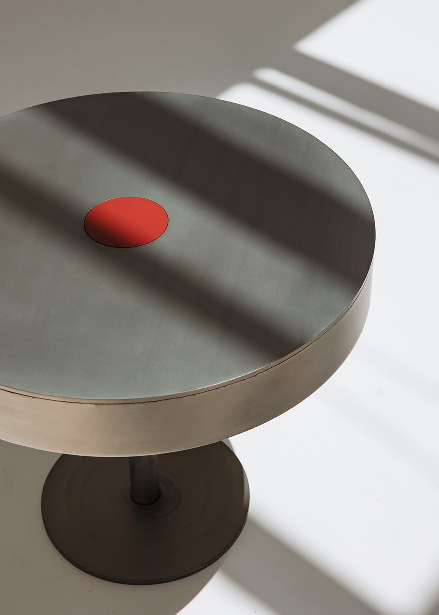 Mesa circular de centro realizada en acero con acabado mate y detalle lacado en rojo en el centro.