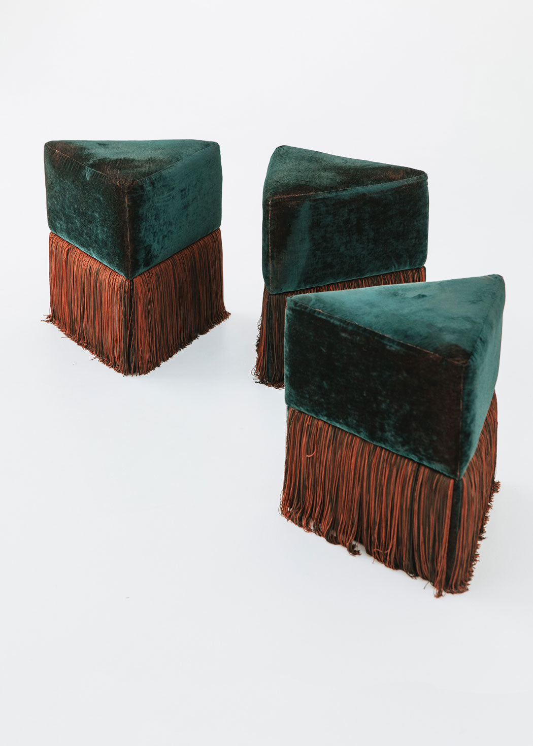 Puf triangular tapizado en terciopelo azul con detalle de flecos en la parte inferior.