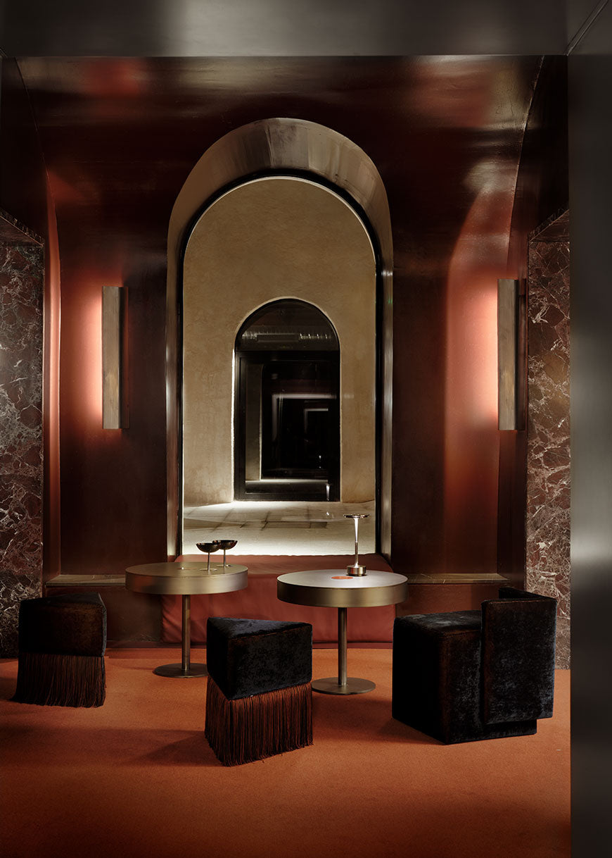 Puf cuadrado tapizado en terciopelo azul con detalle de flecos en la parte inferior.