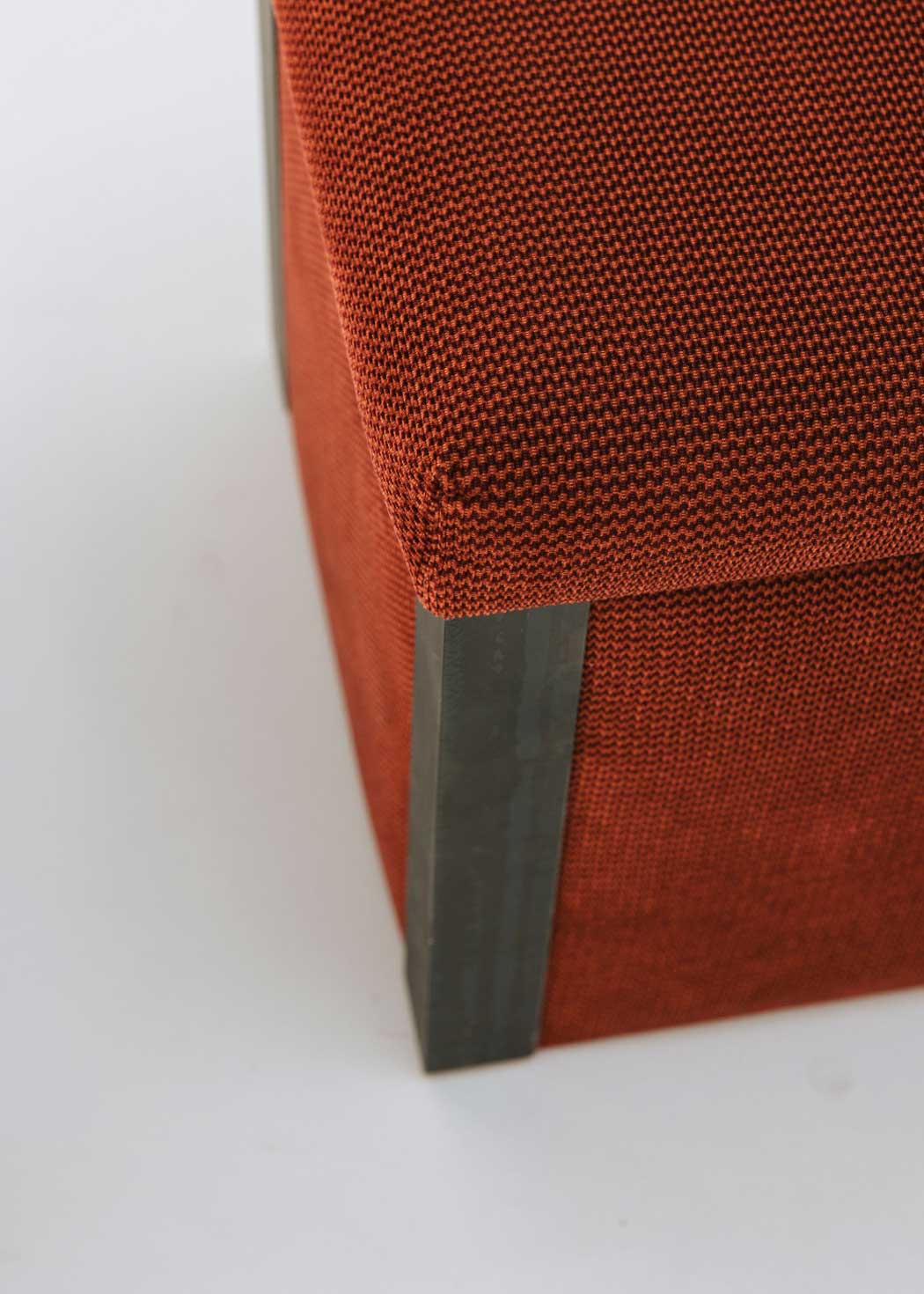 Puf cuadrado tapizado en terciopelo rojo con remates laterales de acero inoxidable.