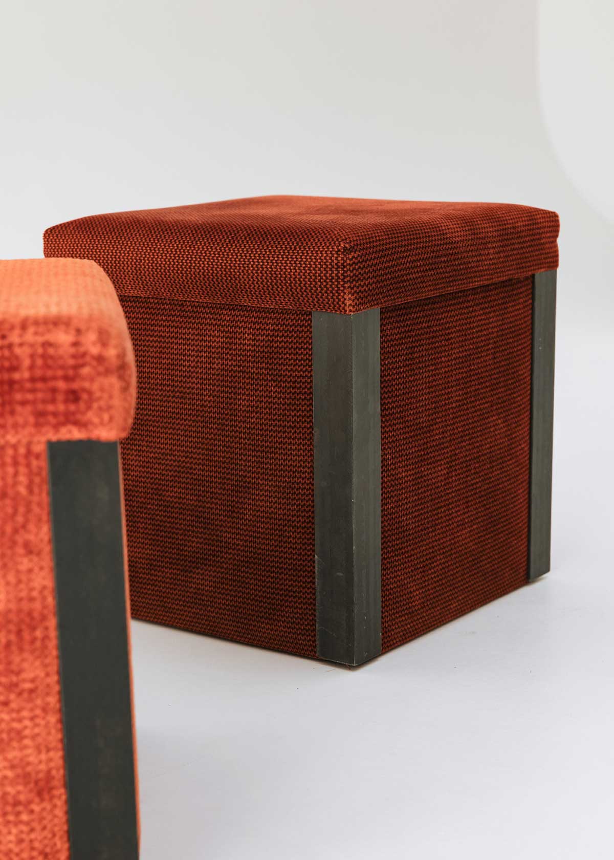 Puf cuadrado tapizado en terciopelo rojo con remates laterales de acero inoxidable.