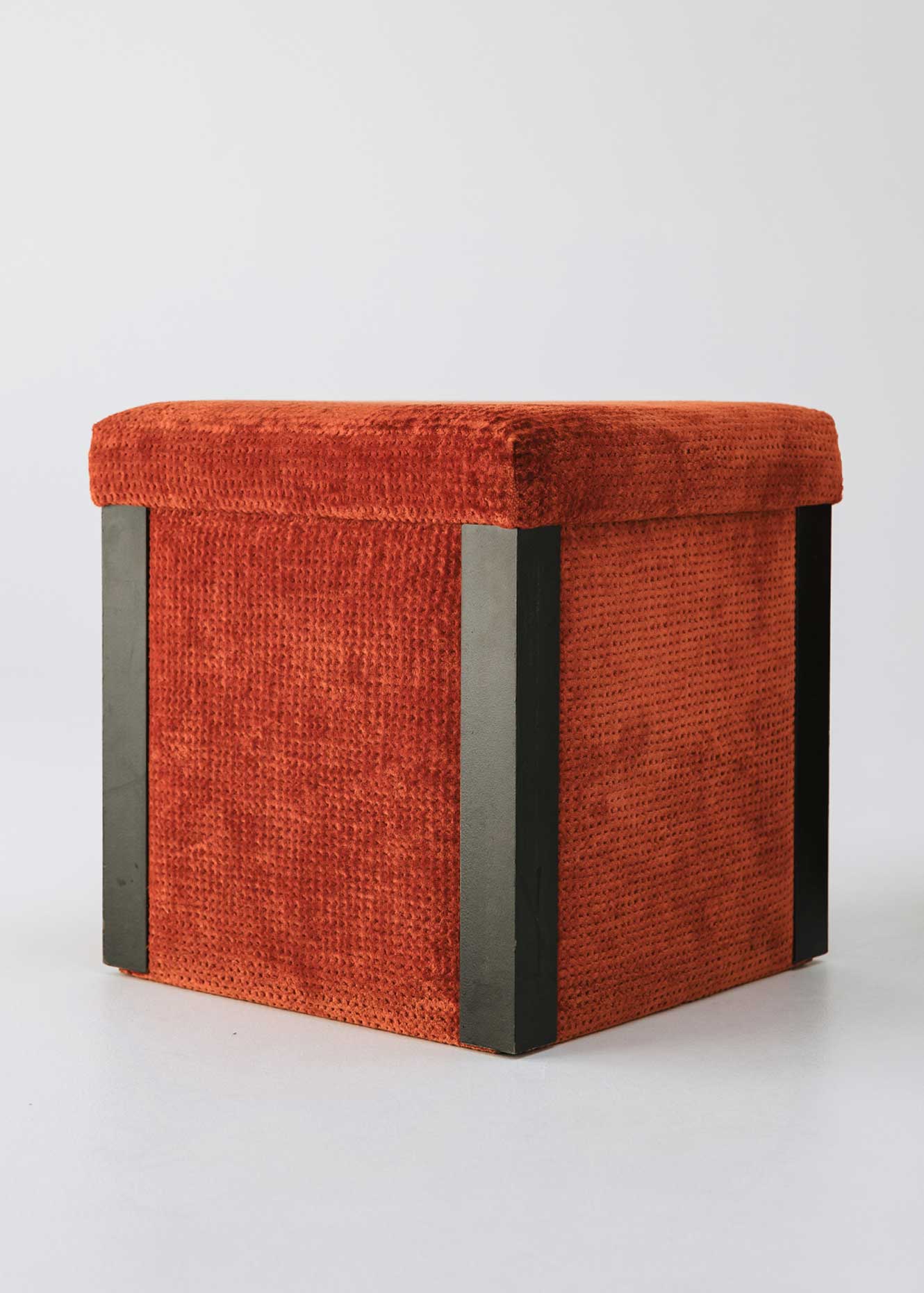 Puf cuadrado tapizado en terciopelo rojo con remates laterales de acero inoxidable.