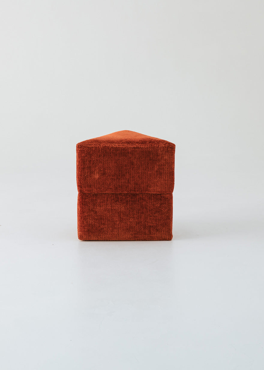 Puf triangular tapizado en tejido en tonos rojos, morados y burdeos.