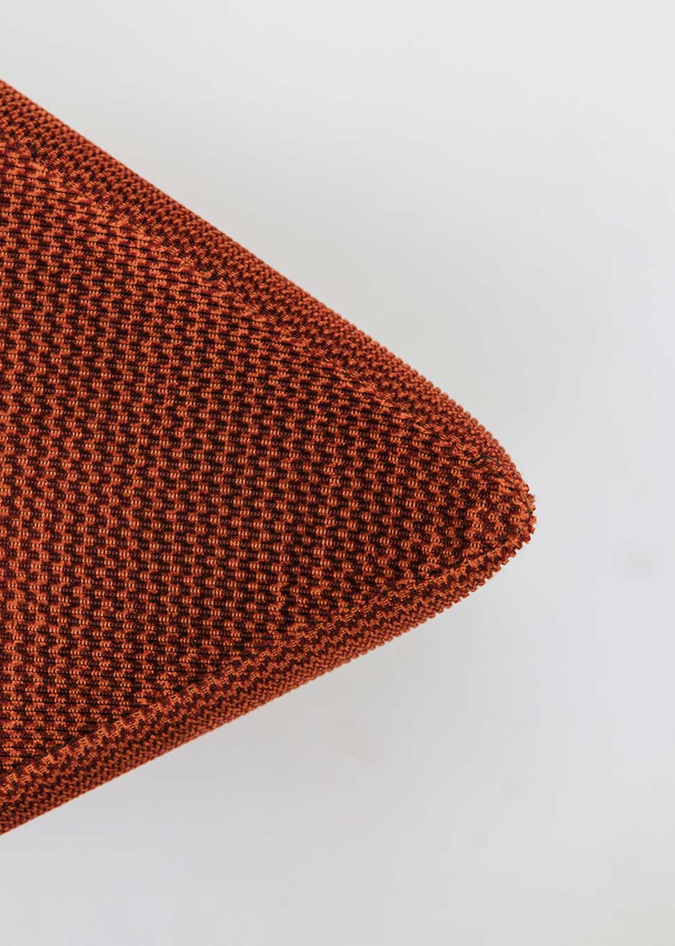 Puf triangular tapizado en tejido en tonos rojos, morados y burdeos.