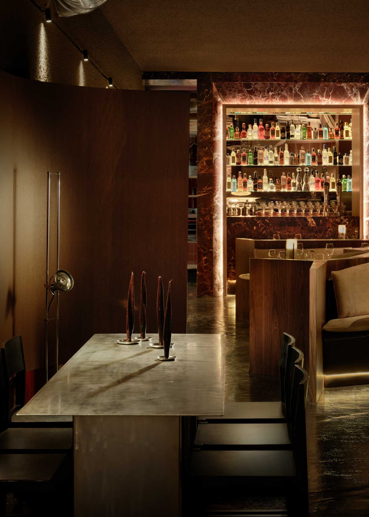 Mesa de comedor rectangular con estructura metálica de acero inoxidable cepillado para patas y sobre. Una de las patas va lacada en rojo.