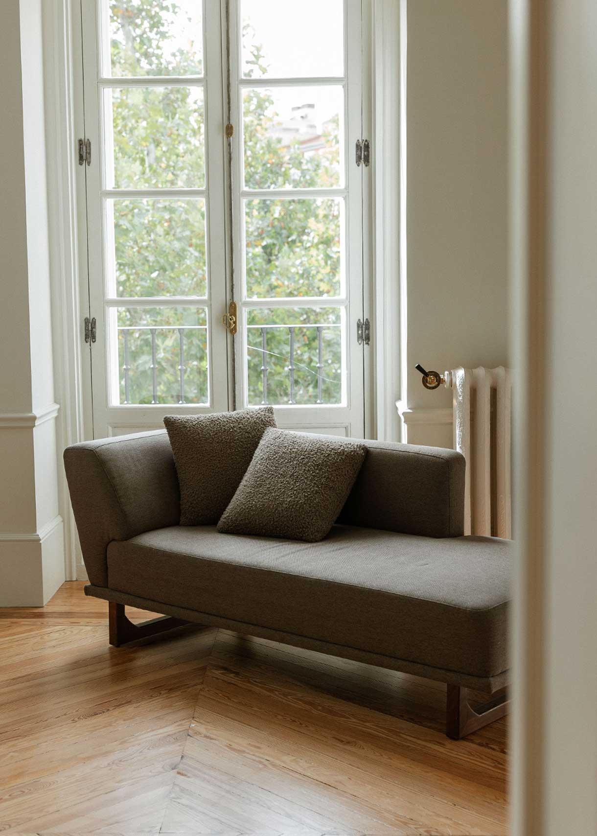 Diván con estructura y patas de madera tapizado con tela gris. Incluye almohadones con relleno en fibra.