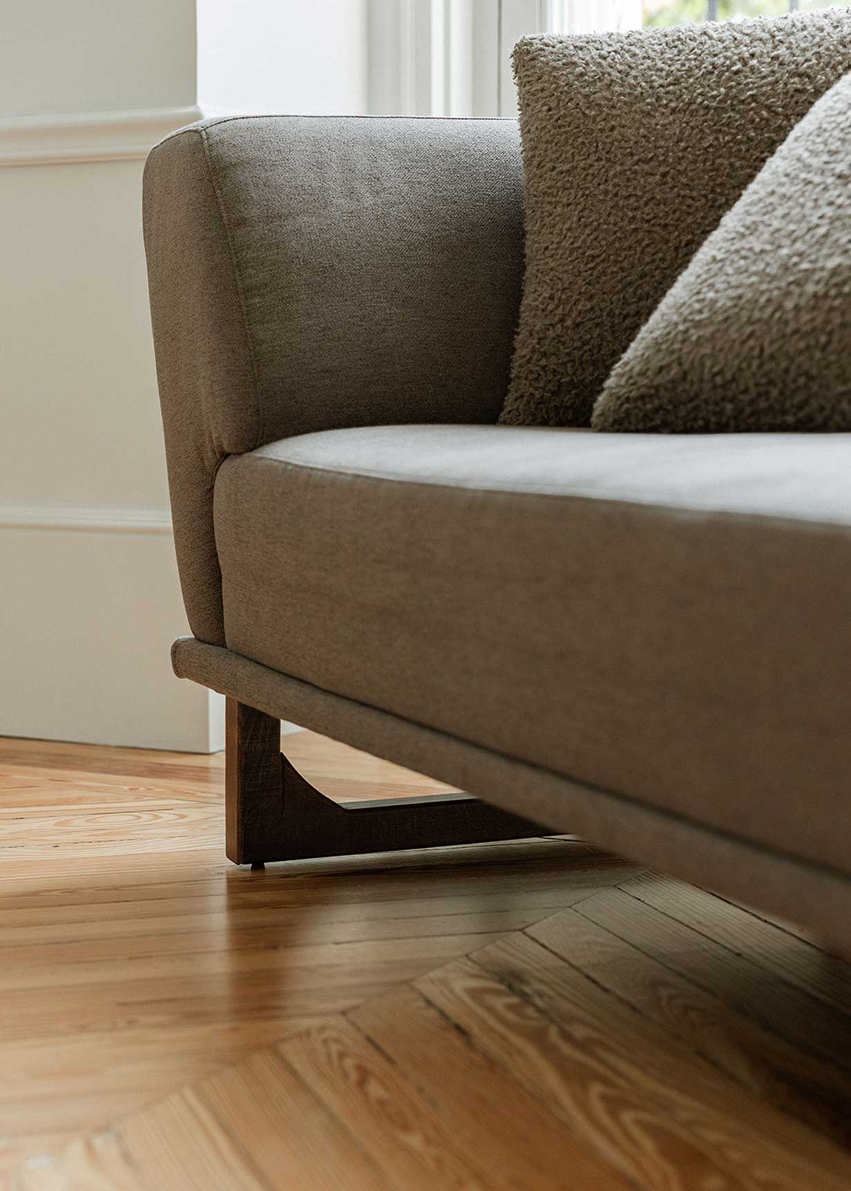 Diván con estructura y patas de madera tapizado con tela gris. Incluye almohadones con relleno en fibra.