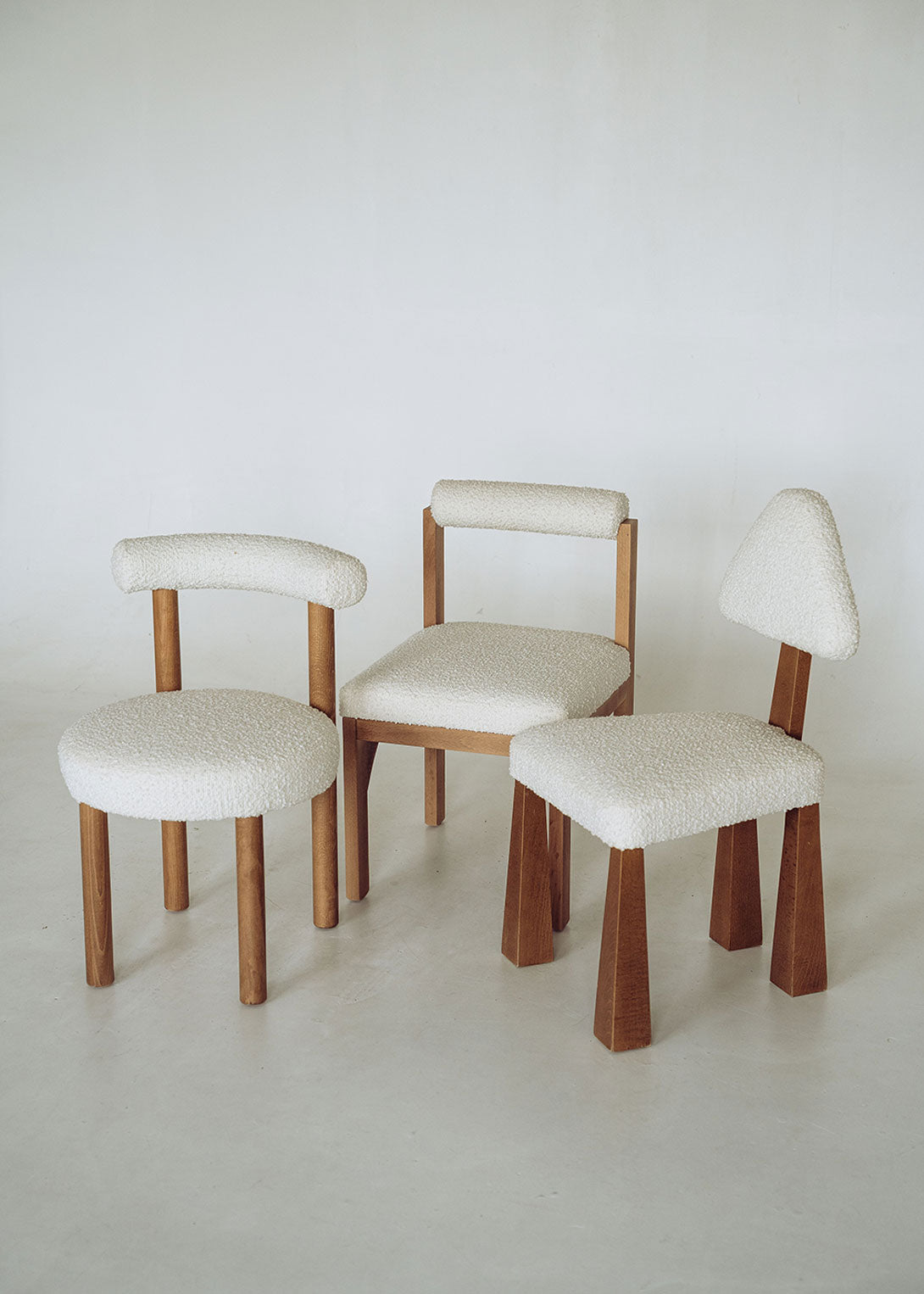 Silla de madera de haya tapizada en bouclé blanco con respaldo semicircular.