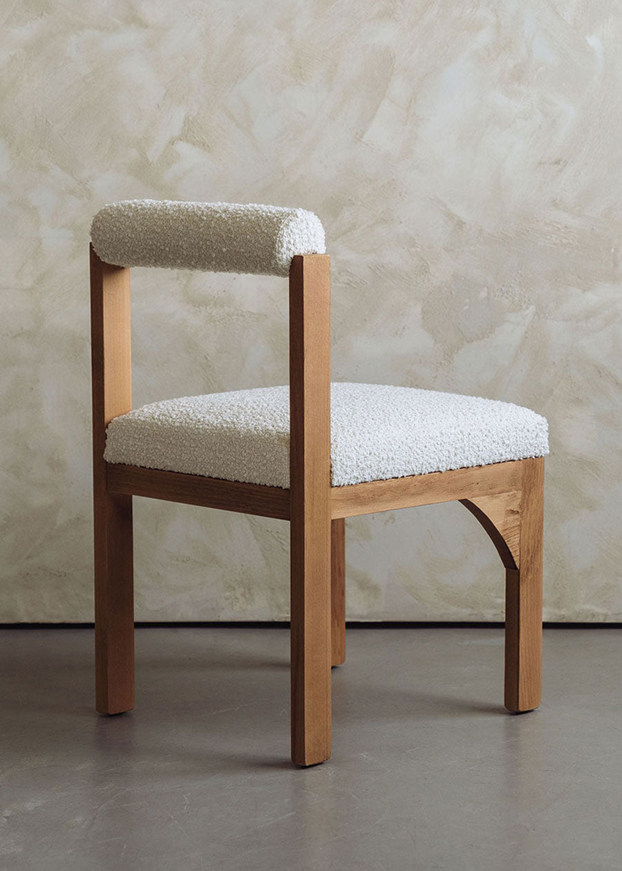 Silla de madera de haya tapizada en bouclé blanco con respaldo cilíndrico.