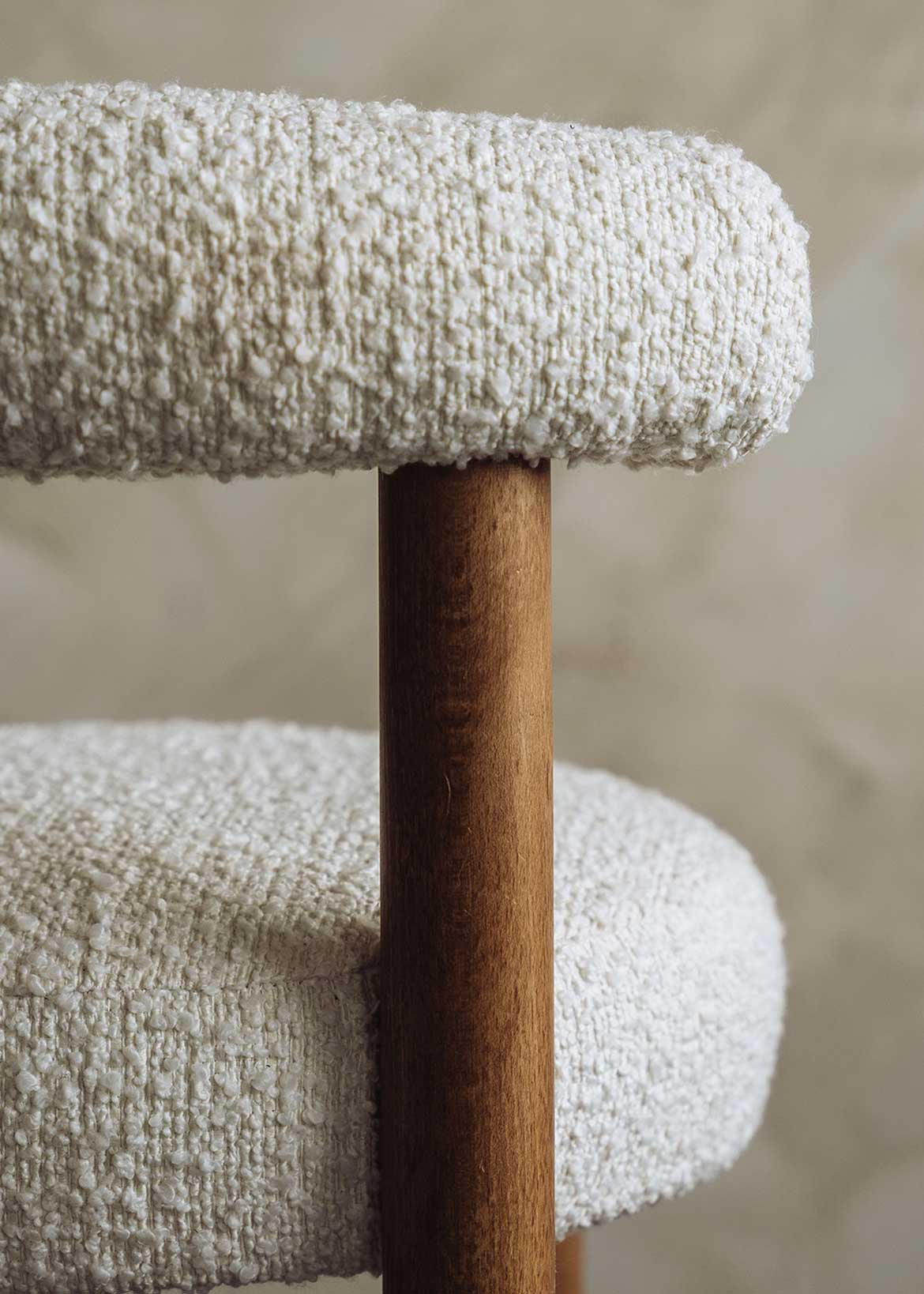 Taburete tapizado en tela beige con estructura de madera de haya. Un taburete alto con respaldo semicircular y reposapiés con acabado de latón incorporado.