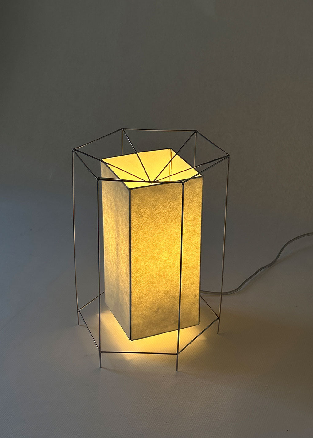 La lámpara CM58 tiene estructura de paraguas. Sus varillas metálicas que conforman su esqueleto evocan esas formas geométricas y modulares que permitieron levantar una arquitectura desmontable, flexible y profundamente moderna.
