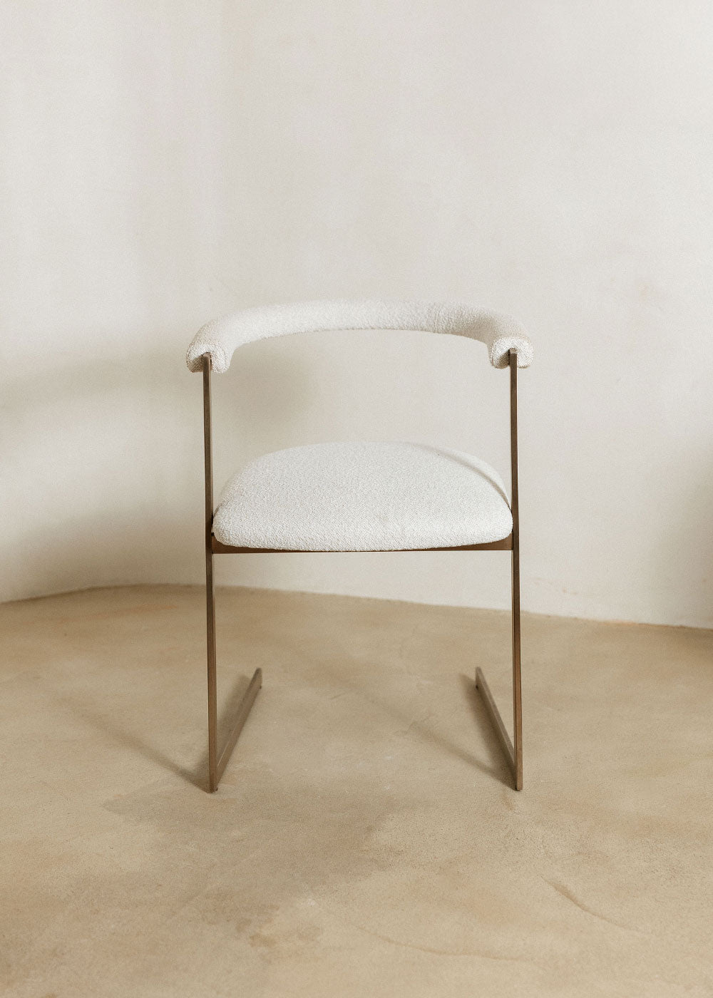 Silla de latón con acabado cepillado, tapizada con bouclé blanco.