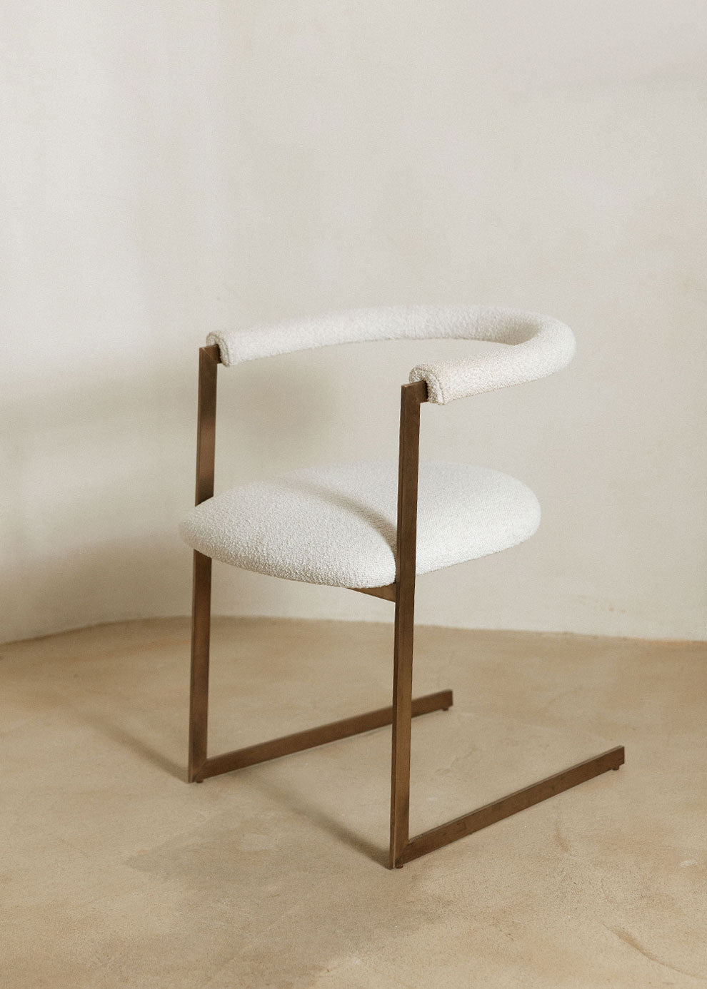 Silla de latón con acabado cepillado, tapizada con bouclé blanco.