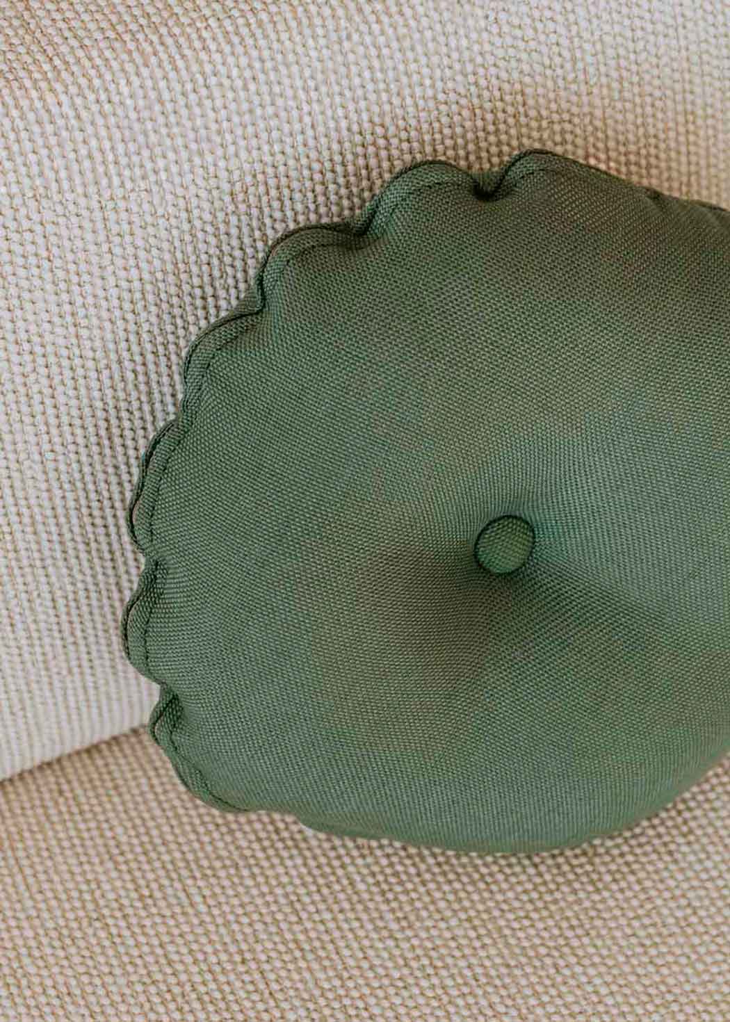 Almohadón circular con capitoné, tapizado en tela verde.