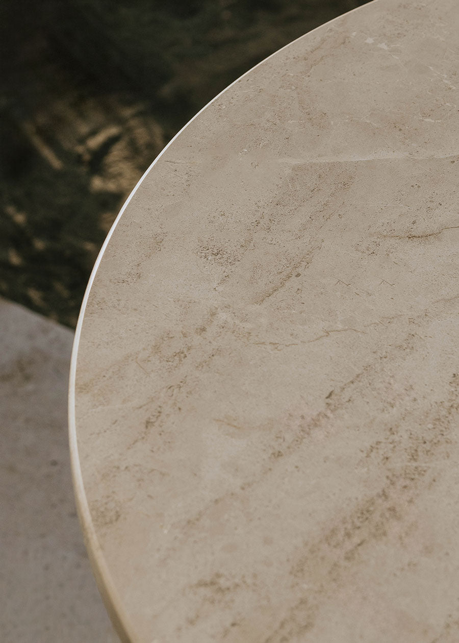 Mesa alta de exterior circular con estructura de tres pies cruzados de hierro forjado acabado en negro y sobre de mármol crema marfil.