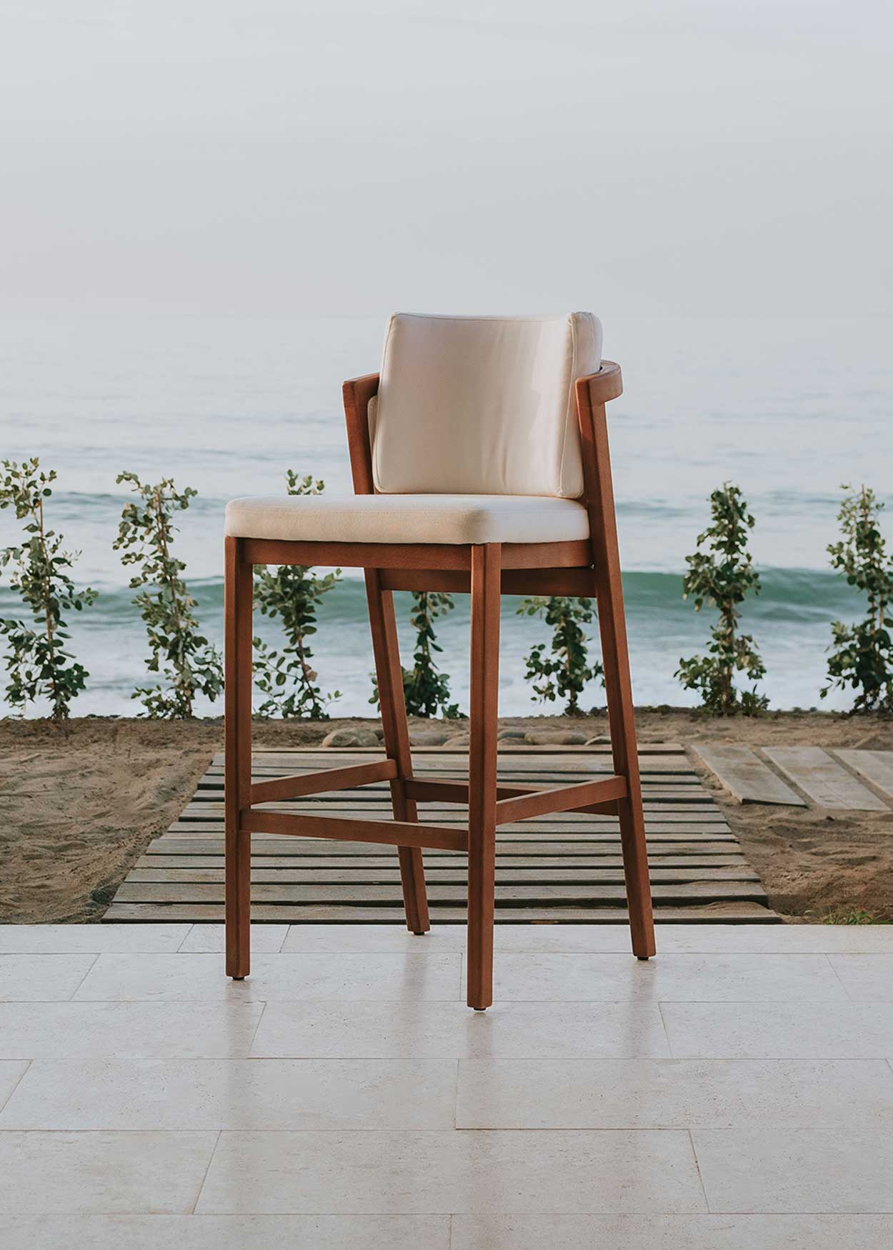 Taburete de exterior en madera de haya con respaldo tapizado en tela blanca.