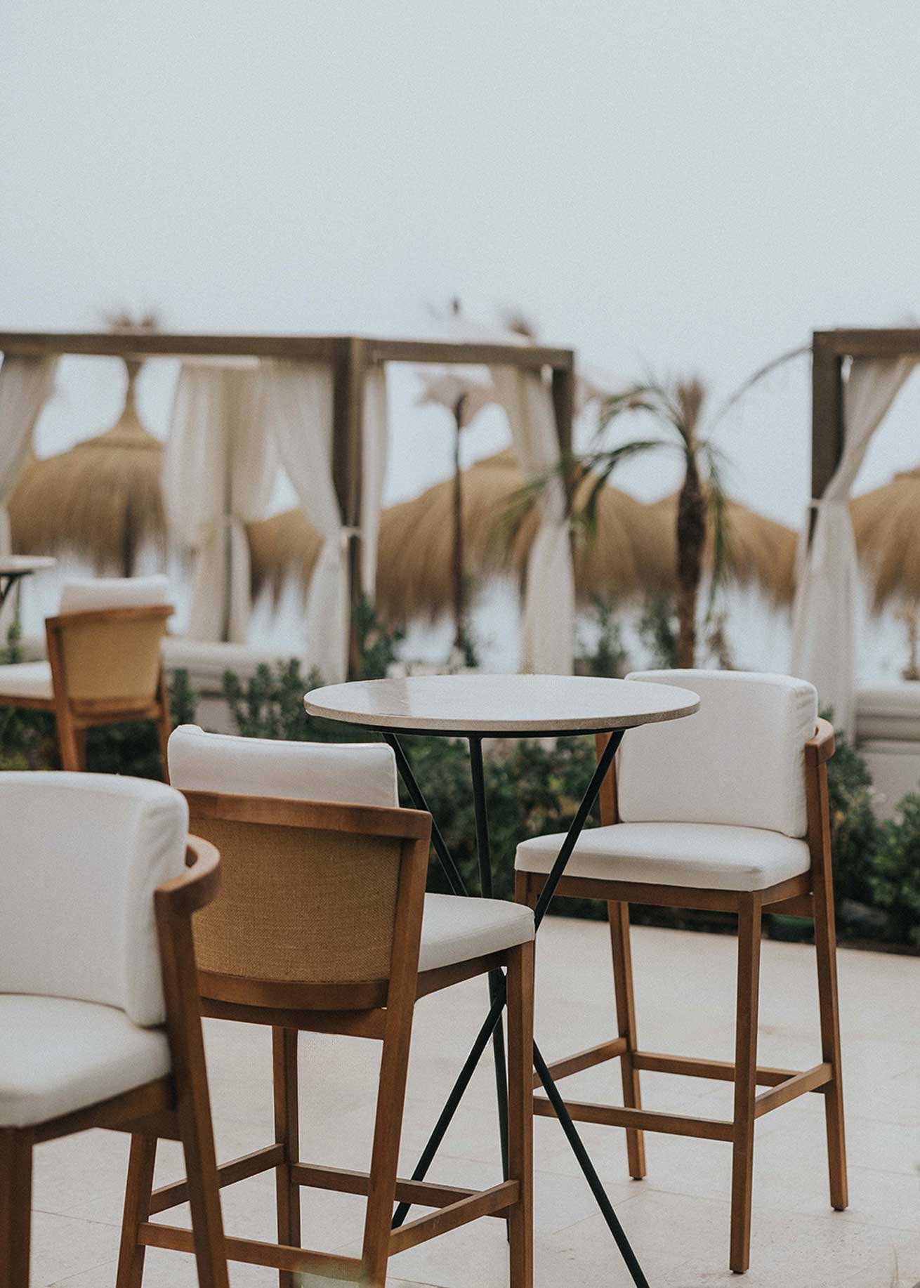 Taburete de exterior en madera de haya con respaldo tapizado en tela blanca.