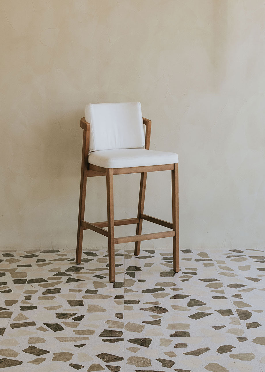 Taburete de exterior en madera de haya con respaldo tapizado en tela blanca.