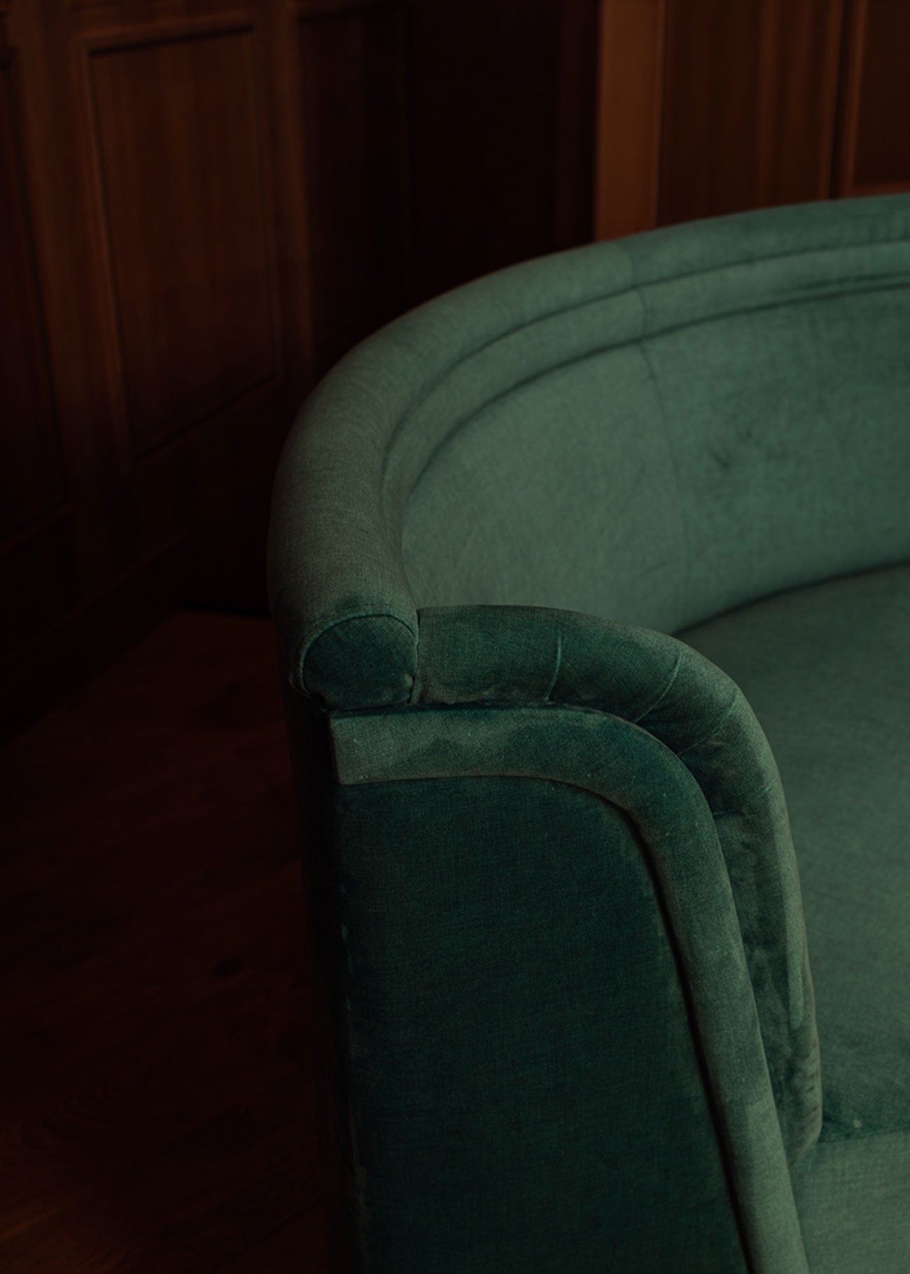 Banco curvado tapizado en terciopelo verde con patas de madera de haya.